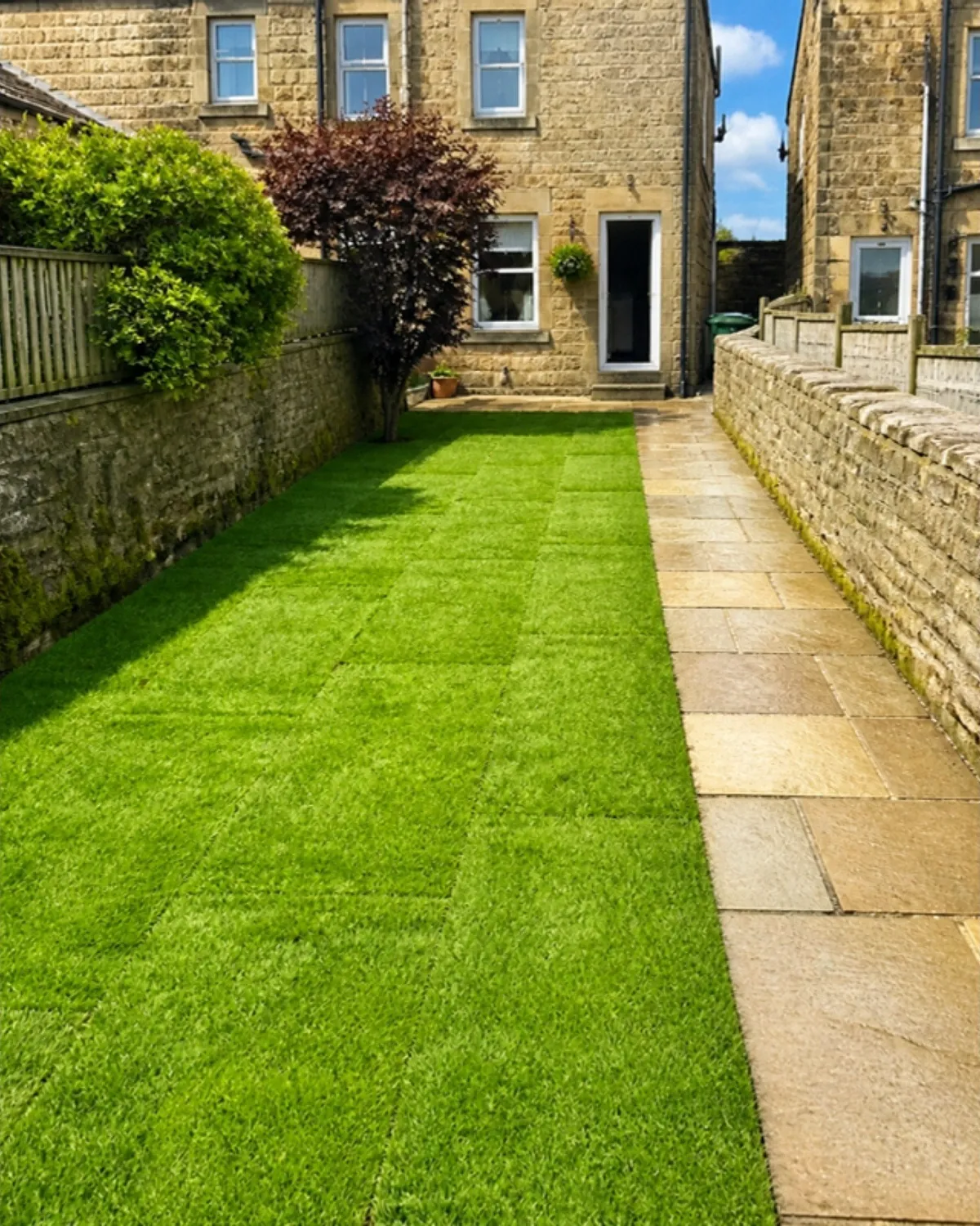 Long, narrow back garden of a stone terraced house with new turf beside a flagstone path
