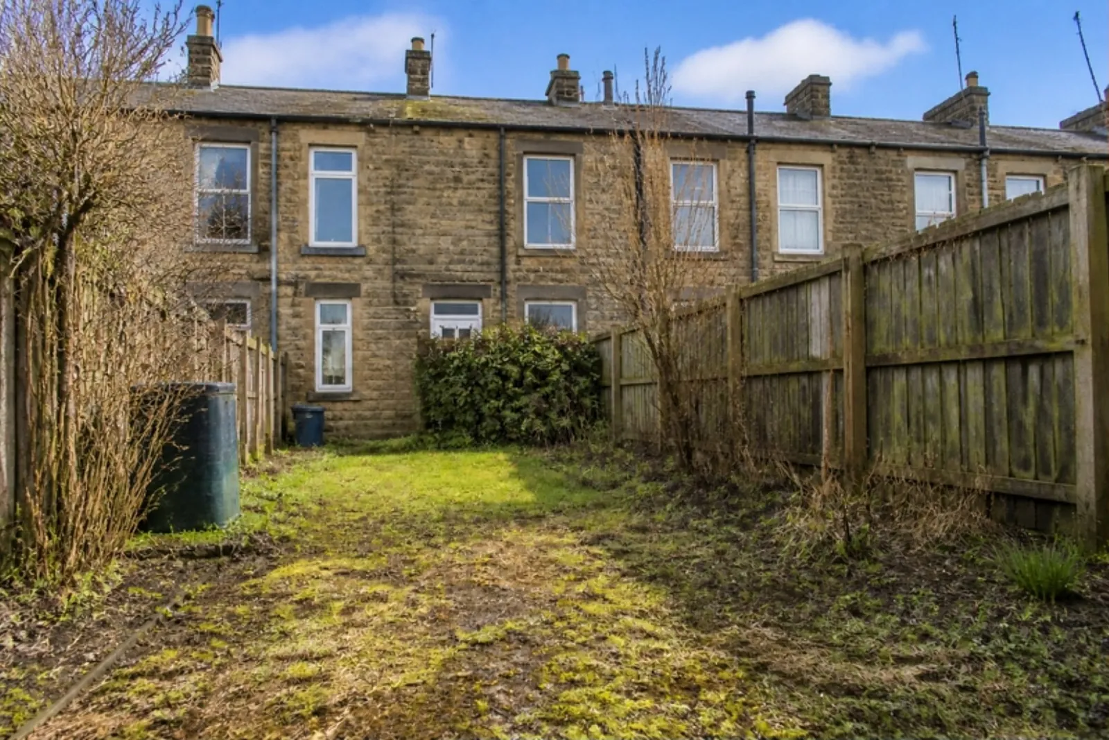 Neglected back garden behind a stone terrace, with mossy, patchy grass and bare muddy patches
